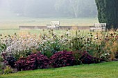 GLYNDEBOURNE, EAST SUSSEX: THE MAIN LAWN WITH BENCHES AND YEWS, BORDER WITH SEDUMS AND GAURA LINDHEIMERI - COUNTRY GARDEN, SUMMER
