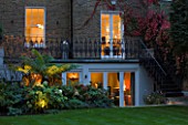 NOTTING HILL HOUSE, LONDON. GARDEN DESIGN BY BUTTER WAKEFIELD. VIEW OF REAR OF HOUSE & BORDER WITH BALCONY. UPLIGHTING ON TREE FERN AND HYDRANGEAS.NIGHT,EVENING,LIT,GLOW,DUSK