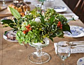 COMMON FARM FLOWERS. SOMERSET: FOOTED GLASS CANDLE CENTRE PIECE ARRANGEMENT MADE UP OF BRITISH GROWN FLOWERS AND FOLIAGE; HYDRANGEA HEADS  VIBURNUM DAVIDII  HOLLY AND HIPS.