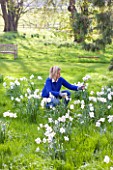 EASTON WALLED GARDEN  LINCOLNSHIRE:  URSULA CHOLMELY IN THE MEADOW SURROUNDED BY NARCISSUS POETICUS RECURVUS - PHEASANTS EYE NARCISSUS - DAFFODILS  WHITE FLOWERS. SPRING.