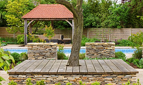 ARALIA_GARDEN_DESIGN__PATRICIA_FOX_WEDNESDAY_HOUSE_WOODEN_TREE_SEAT_WITH_STONE_WALL_AND_WOODEN_LOGGI