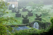 ROCKCLIFFE HOUSE, GLOUCESTERSHIRE: GATE IN WALL WITH YEW TOPIARY BIRDS LEADING TO STONE DOVECOT - CLIPPED, EVERGREEN, GREEN, FOG, MIST, SUMMER