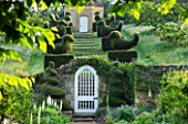 ROCKCLIFFE HOUSE, GLOUCESTERSHIRE: BORDER WITH GRAVEL PATH LEADING UP TO WHITE GATE IN WALL WITH TOPIARY BIRDS LEADING UP TO DOVECOT. COUNTRY GARDEN, SUMMER