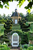 ROCKCLIFFE HOUSE, GLOUCESTERSHIRE: VIEW THROUGH WHITE GATE TO ROW OF CLIPPED TOPIARY BIRDS LEADING UP TO DOVECOTE. SUMMER, COUNTRY GARDEN