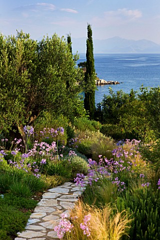 CORFU_GREECE__THE_KASSIOPIA_ESTATE_VIEW_OUT_TO_SEA_FROM_GARDEN_WITH_STONE_PATH__STIPA_TENUISSUIMA_TU