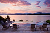CORFU, GREECE - THE KASSIOPIA ESTATE: EVENING LIGHT - DUSK ON THE TERRACE LOOKING OUT TO SEA WITH SUN LOUNGERS. IN THE DISTANCE ARE THE ALBANIAN MOUNTAINS