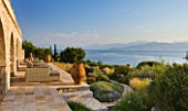 CORFU, GREECE - THE KASSIOPIA ESTATE: THE STONE TERRACE WITH SEATING AREA, GARDEN, TERRACOTTA URNS AND VIEW OUT TO SEA