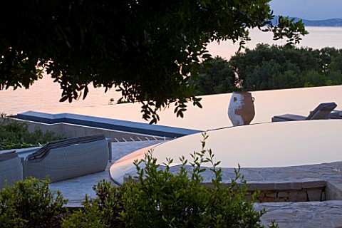 CORFU_GREECE__THE_KASSIOPIA_ESTATE_EVENING_LIGHT_ON_INFINITY_POOL_AND_STONE_TERRACE_WITH_TERRACOTTA_