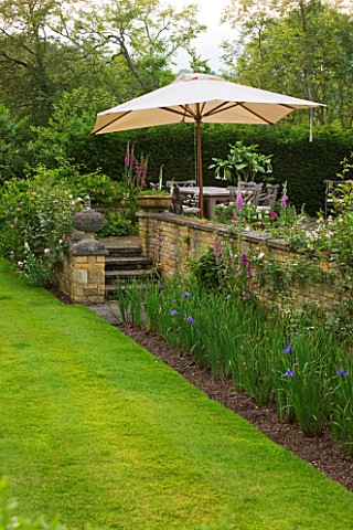 ROCKCLIFFE_HOUSE_GLOUCESTERSHIRE_BORDER_BESIDE_WALL_STEPS_AND_TERRACE_WITH_TABLE_CHAIRS_AND_PARASOL_