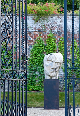 POULTON_HOUSE_GARDEN_WILTSHIRE_WROUGHT_IRON_GATES_AND_STONE_SCULPTURE_IN_THE_WALLED_GARDEN__MARBLE_S