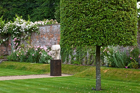 POULTON_HOUSE_GARDEN_WILTSHIRE_WALLED_GARDEN_IN_SUMMER_WITH_ROSES_CLIPPED_QUERCUS_ILEX_TREE_AND_STON