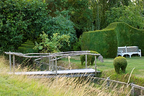 WOOLSTONE_MILL_HOUSE_OXFORDSHIRE_WOODEN_BRIDGE_OVER_STREAM_WITH_YEW_HEDGE_AND_BENCH_A_PLACE_TO_SIT
