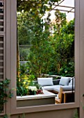 PRIVATE GARDEN LONDON: DESIGNER STEPHEN WOODHAMS - TOWN GARDEN - BACK GARDEN VIEW OUT OF CONSERVATORY WINDOW TO SEATING ON TERRACE OUTSIDE