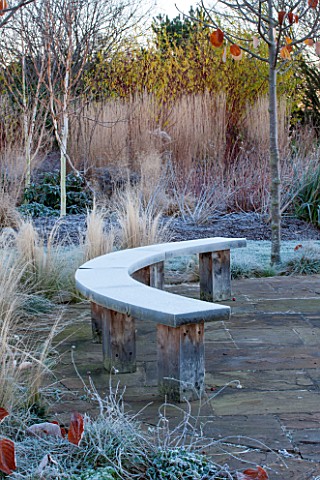 ELLICAR_GARDENS_NOTTINGHAMSHIRE_PAVED_PATIO_AREA_BESIDE_POOL_WITH_CURVED_WOODEN_BENCH_SEAT