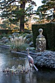 SEDGWICK PARK, WEST SUSSEX. COLUMNS OF YEW BESIDE THE LONG CANAL ALSO KNOWN AS THE WHITE SEA WITH PAMPAS GRASS AND RUSTED METAL BIRD. WINTER, GARDEN, FROST, JANUARY, WATER.