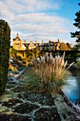 SEDGWICK PARK, WEST SUSSEX IN WINTER. VIEW TO HOUSE WITH FROSTY POND - THE LONG CANAL ALSO KNOWN AS THE WHITE SEA & PAMPAS GRASS. WINTER, FROST, JANUARY, GARDEN, FORMAL, WATER