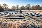 SEDGWICK PARK, WEST SUSSEX. WINTER. GREEK STYLE GRASS LABYRINTH WITH STANDING STONE AND PEA SHINGLE PATH IN FROST. JANUARY, GARDEN.