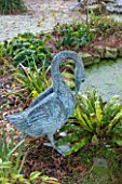 SEDGWICK PARK, WEST SUSSEX. SWAN STATUE/SCULPTURE BESIDE POND COVERED WITH DUCKWEED WITH FERNS. WATER, WINTER, JANUARY, GARDEN