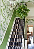 BUTTER WAKEFIELD HOUSE, LONDON. THE HALLWAY AT CHRISTMAS. STAIRS WITH BOLD STRIPED CARPET, PALM FROND WALLPAPER AND KISSING BALL WITH EUCALYPTUS AND PINE