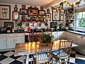 BUTTER WAKEFIELD HOUSE, LONDON. THE KITCHEN AT CHRISTMAS: CANDLES AND TABLE DECORATION WITH SEASONAL FOLIAGE CREATE A FESTIVE FEEL. FRAMED BOTANICAL PRINTS ADD INTEREST TO WALLS.