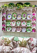 BUTTER WAKEFIELD HOUSE, LONDON. THE GARDEN ROOM AT CHRISTMAS.CONSERVATORY JUST OFF THE KITCHEN WITH SOFA AND BUTTERS CHINA PLATES DISPLAYED ON PLATE RACK.