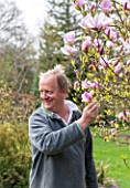 SPINNERS GARDEN AND NURSERY, HAMPSHIRE: ANDREW ROBERTS - OWNER OF SPINNERS NURSERY LOOKING AT MAGNOLIA PINKIE