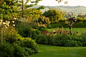 THE OLD VICARAGE, WORMLEIGHTON, WARWICKSHIRE: DESIGNER ANGEL COLLINS - VIEW OF LAWN AND SUNDIAL BED WITH COUNTRYSIDE BEYOND. EVENING LIGHT, CLASSIC COUNTRY GARDEN