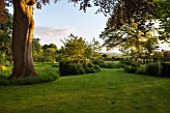 THE OLD VICARAGE, WORMLEIGHTON, WARWICKSHIRE: DESIGNER ANGEL COLLINS - VIEW OF LAWN AND SUNDIAL BED WITH COUNTRYSIDE BEYOND. EVENING LIGHT, CLASSIC COUNTRY GARDEN