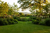 THE OLD VICARAGE, WORMLEIGHTON, WARWICKSHIRE: DESIGNER ANGEL COLLINS - VIEW OF LAWN AND SUNDIAL BED WITH COUNTRYSIDE BEYOND. EVENING LIGHT, CLASSIC COUNTRY GARDEN: