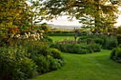 THE OLD VICARAGE, WORMLEIGHTON, WARWICKSHIRE: DESIGNER ANGEL COLLINS - VIEW OF LAWN AND SUNDIAL BED WITH COUNTRYSIDE BEYOND. ALLIUM MOUNT EVEREST IN BORDER. EVENING LIGHT