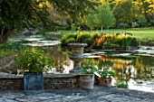 ABLINGTON MANOR  GLOUCESTERSHIRE: VIEW ACROSS COLN RIVER WITH TERRACE AND CONTAINERS WITH REFLECTIONS OF TREES IN WATER. CLASSIC COUNTRY GARDEN  COTSWOLDS  ROMANTIC  ROMANCE