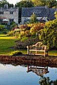 ABLINGTON MANOR  GLOUCESTERSHIRE: VIEW ACROSS RIVER COLN TO WOODEN LUTYENS BENCH / SEAT AND BORDERS BEYOND. CLASSIC COUNTRY GARDEN  SUMMER  JUNE  ROMANCE  ROMANTIC