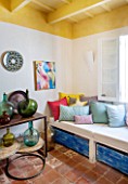 CIUTADELLA MENORCA, SPAIN: EVELYNE MANDEL HOUSE - FRONT ROOM, LIVING ROOM IN BLUE AND YELLOW  - SEAT WITH CUSHIONS - VINTAGE MENORCAN GLASS JARS ON WOODEN TABLES
