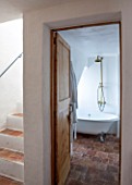 CIUTADELLA MENORCA, SPAIN: EVELYNE MANDEL HOUSE - VIEW THROUGH DOORWAY OF BATHROOM TO ROLL TOP BATH AND STAIRCASE - BRASS SHOWER