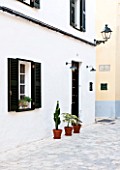 CIUTADELLA MENORCA, SPAIN: EVELYNE MANDEL HOUSE - THE FRONT OF THE HOUSE WITH GREEN SHUTTERS AND SUCCULENTS IN ETRRACOTTA CONTAINERS