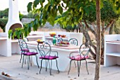 JONATHAN BAILLIE GARDEN, ALAIOR, MENORCA: BUILT IN BARBEQUE AND TABLE WITH METAL CHAIRS, SURROUNDED BY CLIPPED OLIVE TREES. FOOD, DINING, ENTERTAINING AREA, OUTDOOR LIFESTYLE