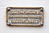 WEST DEAN GARDENS, WEST SUSSEX: DETAIL OF MAKERS NAME PLATE ON THE DOOR OF A GLASSHOUSE / GREENHOUSE ROOF IN THE WALLED KITCHEN GARDEN. AUGUST, CLASSIC COUNTRY GARDEN