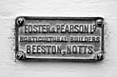 WEST DEAN GARDENS, WEST SUSSEX: BLACK AND WHITE IMAGE OF MAKERS NAME PLATE ON THE DOOR OF A GLASSHOUSE / GREENHOUSE ROOF IN THE WALLED KITCHEN GARDEN. AUGUST
