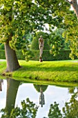 GREAT FOSTERS. SURREY:  SOARING FIGURE - SCULPTURE IN STAINLESS STEEL BY RICK KIRBY BESIDE THE MOAT - WATER, ART, CLASSIC, FORMAL, COUNTRY GAREDEN