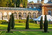 SEZINCOTE, GLOUCESTERSHIRE: THE MAGNIFICENT CURVING ORANGERY WITH CONTAINERS OF FUCHSIAS OUTSIDE IN MORNING LIGHT - TENT AND IRISH YEWS