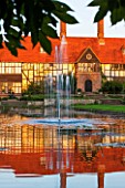 RHS GARDEN, WISLEY, SURREY: THE HOUSE AND LABORATORY AT SUNSET SEEN ACROSS THE CANAL FROM THE LOGGIA, WATER, SUMMER, GARDEN, CLASSIC, FOUNTAIN