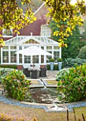 SURREY GARDEN DESIGNED BY ANTHONY PAUL: VIEW TO HOUSE CONSERVATORY WITH CIRCULAR POOL AND RILL - MORNING LIGHT, COUNTRY GARDEN, CLASSIC, SUMMER