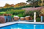 SURREY GARDEN DESIGNED BY ANTHONY PAUL: SWIMMING POOL WITH TERRACE - RATTEN FURNITURE, CUSHIONS, CAREX FLAGELLIFERA IN METAL CONTAINERS. WATER, COUNTRY GARDEN, CLASSIC