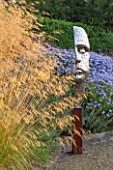 SURREY GARDEN DESIGNED BY ANTHONY PAUL: FOCAL POINT - PIXELATED STYLE STEEL HEAD BY RICK KIRBY WITH STIPA GIGANTEA AND ASTERS BEHIND - SUMMER, SEPTEMBER, COUNTRY GARDEN