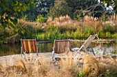 ELLICAR GARDENS, YORKSHIRE - DESIGNER SARAH MURCH - NATURAL SWIMMING POOL / POND IN AUTUMN. OCTOBER - VIEW ACROSS DECKING WITH DECKCHAIRS TO POND WITH WOODEN GAZEBO