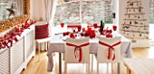 SALTWATER, NORFOLK : DESIGNER KAREN MOORE - CHRISTMAS, DECEMBER, WINTER - THE DINING ROOM IN RED AND WHITE - CORK MIRROR, TABLE AND CHAIRS, RADIATOR, RIBBONS, DECORATION, LIGHTS
