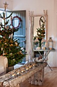 SALTWATER, NORFOLK : DESIGNER KAREN MOORE - CHRISTMAS, DECEMBER, WINTER - WHITE LIVING ROOM - WOODEN TABLE WITH CANDLES, CHRISTMAS TREE, DOOR WITH WREATH - MIRROR, DECORATION