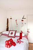 SALTWATER, NORFOLK : DESIGNER KAREN MOORE - CHRISTMAS, DECEMBER, WINTER - BEDROOM IN RED AND WHITE - BED WITH STOCKINGS ON WALL, TOY BOAT AND REINDEERS, ORNAMENT