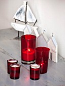 SALTWATER, NORFOLK : DESIGNER KAREN MOORE - CHRISTMAS, DECEMBER, WINTER - BEDROOM IN RED AND WHITE - GREY TABLE WITH RED CANDLES AND WOODEN BOAT ORNAMENT - LIGHTS, LIGHTING