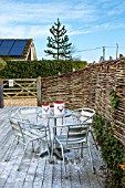 SALTWATER, NORFOLK : DESIGNER KAREN MOORE - CHRISTMAS, DECEMBER, WINTER - DECKED TERRACE OUTSIDE WITH METAL TABLE AND CHAIRS - SNOW, FESTIVE, FENCE, FENCING, WILLOW, WICKER